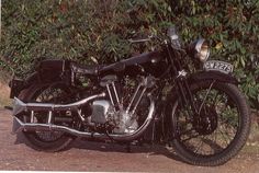 an old motorcycle is parked on the side of the road next to some shrubbery