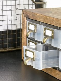 two clear drawers with gold handles on top of a wooden table next to a black and white checkered wall