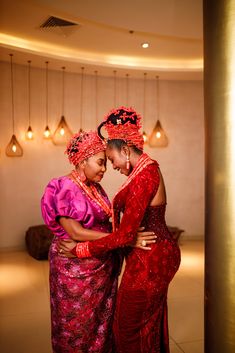 two women dressed in red and pink embrace each other as they pose for the camera