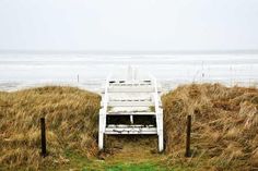 a white chair sitting on top of a grass covered field next to the ocean and beach