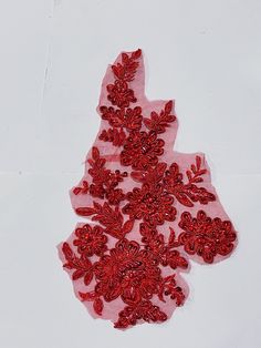 an embroidered piece of fabric with red flowers on it, sitting on a white surface