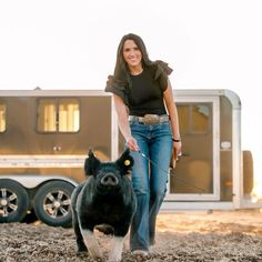 a woman walking a pig on a leash in front of a trailer with a trailer behind her