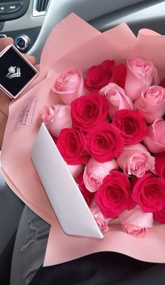 a person holding a bouquet of pink roses in their hand and a cell phone on the dashboard