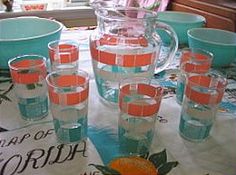 a pitcher and six glasses on a table with oranges in the bowl next to it