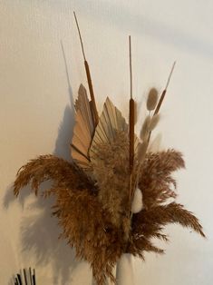 a vase filled with dried flowers on top of a wooden table next to a white wall