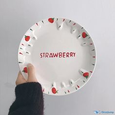 a person holding a white plate with strawberries on it that says strawberry written in red