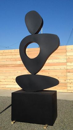 a large metal sculpture sitting on top of a black box next to a wooden fence