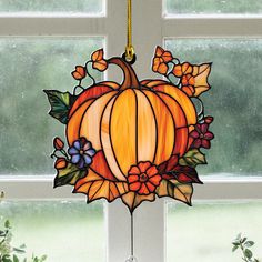 a stained glass pumpkin hanging from the side of a window with flowers and leaves on it