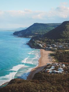 an aerial view of the beach and ocean with houses in the foreground, surrounded by mountains