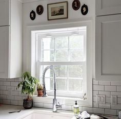 a kitchen with white cabinets and a window above the sink that has a potted plant next to it