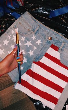 someone is holding a paintbrush in front of an american flag cut out from jean shorts