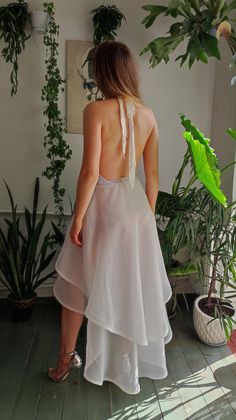 a woman in a white dress is looking down at her back while standing next to some potted plants