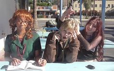 three women sitting at a table with a book and pen in front of their faces