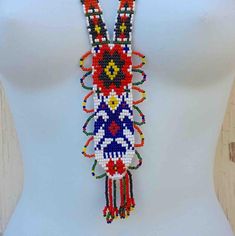 "This long necklace is composed of tiny multicolored beads that are in a narrow formation along neck, then get wider towards the bottom. Main beaded colors are red, blue, orange, and yellow. Sunburst loops near bottom with a fringe of six beaded rows hanging. No clasp or closure, this handmade piece goes right around neck. In good vintage condition. Any questions, Please inquire & Thanks for looking! measures total length- 18\" bottom width- 2 & 1/4\"" Hand-strung Multicolor Beaded Lariat Necklace, Multicolor Southwestern Beaded Necklace With Beaded Chain, Multicolor Bohemian Lariat Beaded Necklace, Bohemian Multicolor Lariat Beaded Necklace, Multicolor Southwestern Beaded Necklace, Multicolor Southwestern Style Beaded Necklace, Southwestern Multicolor Beaded Necklace, Multicolor Southwestern Beaded Chain Jewelry, Multicolor Southwestern Style Beaded Chain Jewelry