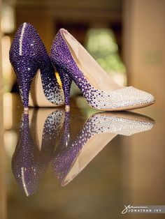 purple and white high heeled shoes sitting on top of a reflective surface in front of a fireplace