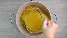 a person pouring liquid into a pot filled with vegetables