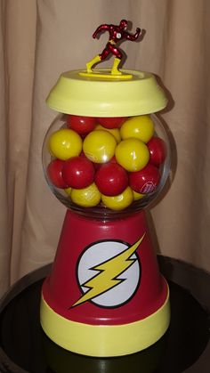 a red and yellow gummy machine with a flash man figure in it's top