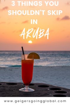 a drink sitting on top of a wooden table next to the ocean with text overlay that reads 3 things you shouldn't skip in aruba