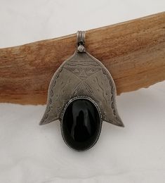 A great Berber Tuareg Khamsa pendant reinterpreted. Featuring the inverted Khamsa / Hand of Fatima, with a large piece of onyx set in place of the central 3 fingers. The large oval cabochon is polished to a high shine and is framed by hand carved silver accented with niello pigment..  The carvings are in the traditional Tuareg geometry of triangles, parallel lines and curves (symbolising nomadic tents, drifting desert sands & animal tracks).  In the Tuareg tradition, silver-smithing is man's work and being a nomadic people, their jewelry is multifunctional by necessity: simultaneously decorative, talismanic and practical.  Weight: 22,5 grams Shipping : DHL EXPRESS 🙂 Artisan Black Ceremonial Jewelry, Traditional Black Medallion Necklace, Artisan Black Engraved Necklace, Traditional Black Engraved Necklace, Traditional Black Medallion Shaped Jewelry, Traditional Black Necklaces With Large Pendant, Traditional Black Necklace With Large Pendant, Animal Tracks, Parallel Lines