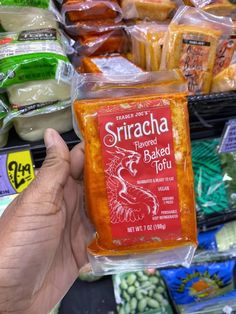 a hand holding up a bag of sliced baked tofu in front of other packaged food items