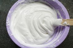 a purple bowl filled with white cream on top of a black counter next to a wooden spoon