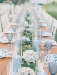 a long table is set with blue and white dishes, candles, and flower centerpieces