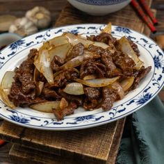 beef and onion stir fry on a blue and white plate with chop sticks in the background