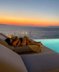 a woman laying on top of a bed next to the ocean at sunset or dawn