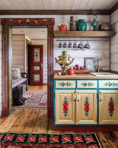 an old fashioned kitchen with wooden floors and painted cupboards on the wall, along with colorful rugs