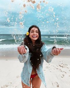 a woman standing on top of a sandy beach next to the ocean holding her arms out