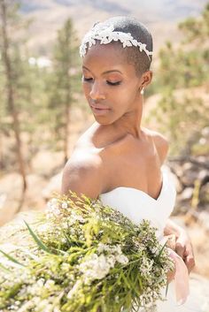 a woman in a wedding dress holding a bouquet of flowers and greenery with mountains in the background