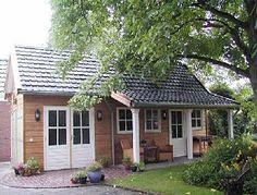 a small wooden house sitting next to a lush green tree in front of a brick building