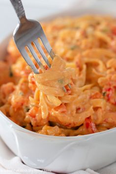 a fork full of macaroni and cheese in a white dish