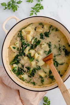 a pot filled with soup and vegetables on top of a white counter next to a wooden spoon