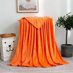 an orange blanket sitting on top of a white floor next to a potted plant