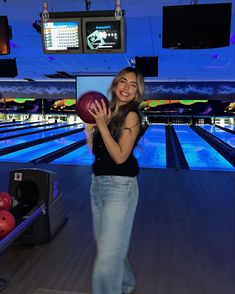 a woman holding a bowling ball in her right hand and smiling at the camera while standing on a bowling alley