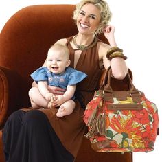 a woman sitting in a chair holding a baby and a handbag on her lap