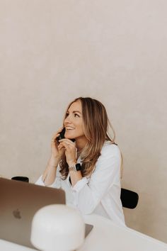 a woman sitting in front of a laptop computer talking on her cell phone and smiling