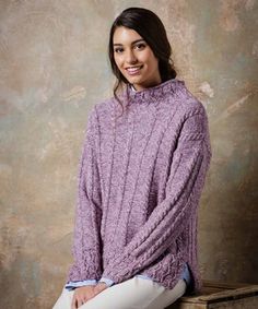 a woman sitting on top of a wooden box wearing a purple sweater and white pants