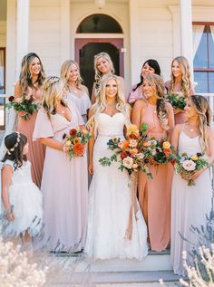 a group of bridesmaids standing in front of a white house with their bouquets