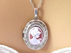 "Romantic Victorian cameo locket necklace with a pendant of a neoclassical woman and flowers against a burgundy red cameo background. The cameo is set in a light weight oval silver plated locket decorated with outer etchings, and you have your choice of a shiny silver finish (shown), gunmetal, and antiqued silver. Also available in gold or bronze. The open locket can hold 2 pictures, and hangs on a rhodium (white gold) plated chain. Length: 18 inches, Locket Pendant: 1.5 inches Please leave a no Elegant Locket Necklace As Gift, Elegant Locket Necklace For Gift, Elegant Medallion Locket Necklace, Elegant Wedding Locket Necklace, Formal Round Pendant Locket Necklace, Elegant Oval Pendant Locket Necklace For Wedding, Elegant Round Pendant Locket Necklace For Wedding, Elegant Oval Locket Necklace For Wedding, Elegant Wedding Locket Necklace With Round Pendant