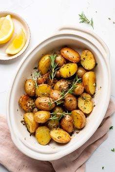 a white bowl filled with potatoes next to a lemon and rosemary garnish on top of a pink napkin