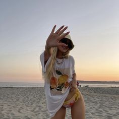 a woman standing on top of a sandy beach next to the ocean holding her hand up