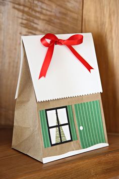 a paper bag with a house on it and a red ribbon tied around the top