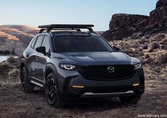 the front end of a gray mazda suv parked on a dirt road with mountains in the background