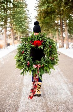 a woman is holding a wreath on the road while wearing boots and a beanie