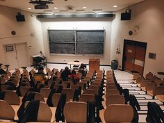 an empty lecture hall with people sitting at tables and chairs in front of the chalkboard