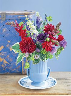 a blue vase filled with lots of flowers on top of a wooden table next to an old suitcase