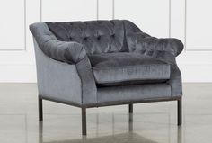 a gray velvet chair sitting on top of a hard wood floor next to a white wall