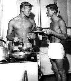 two men standing in a kitchen with pots and pans on the stove, one holding a plate